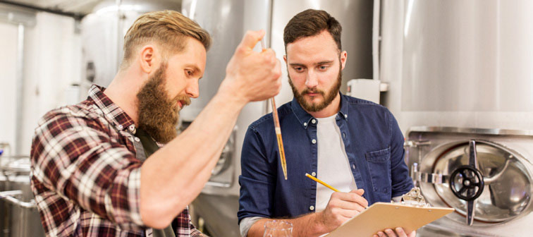 men with pipette testing craft beer at brewery